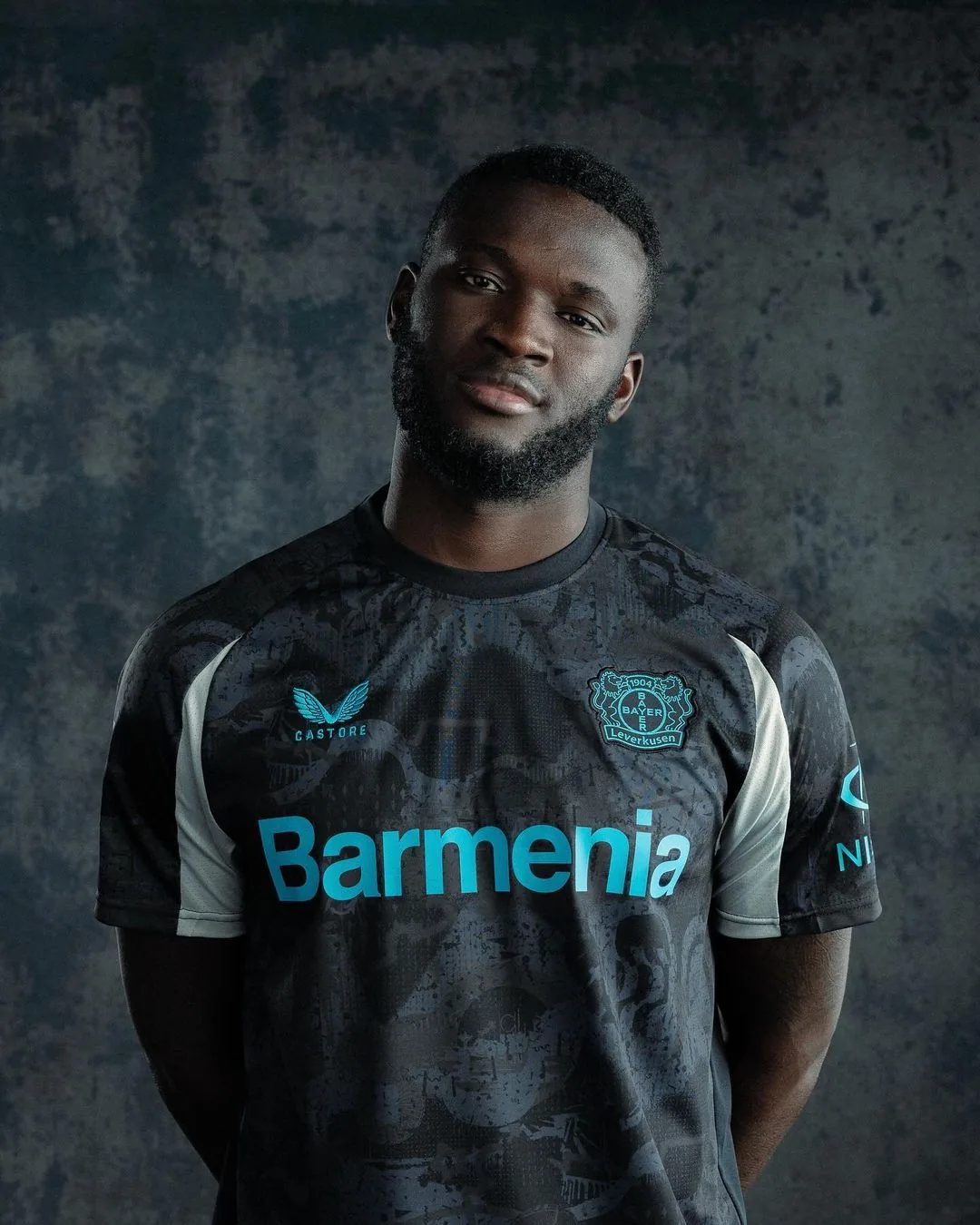 Spieler im Third Jersey von Bayer 04 Leverkusen vor dunklem, strukturiertem Hintergrund